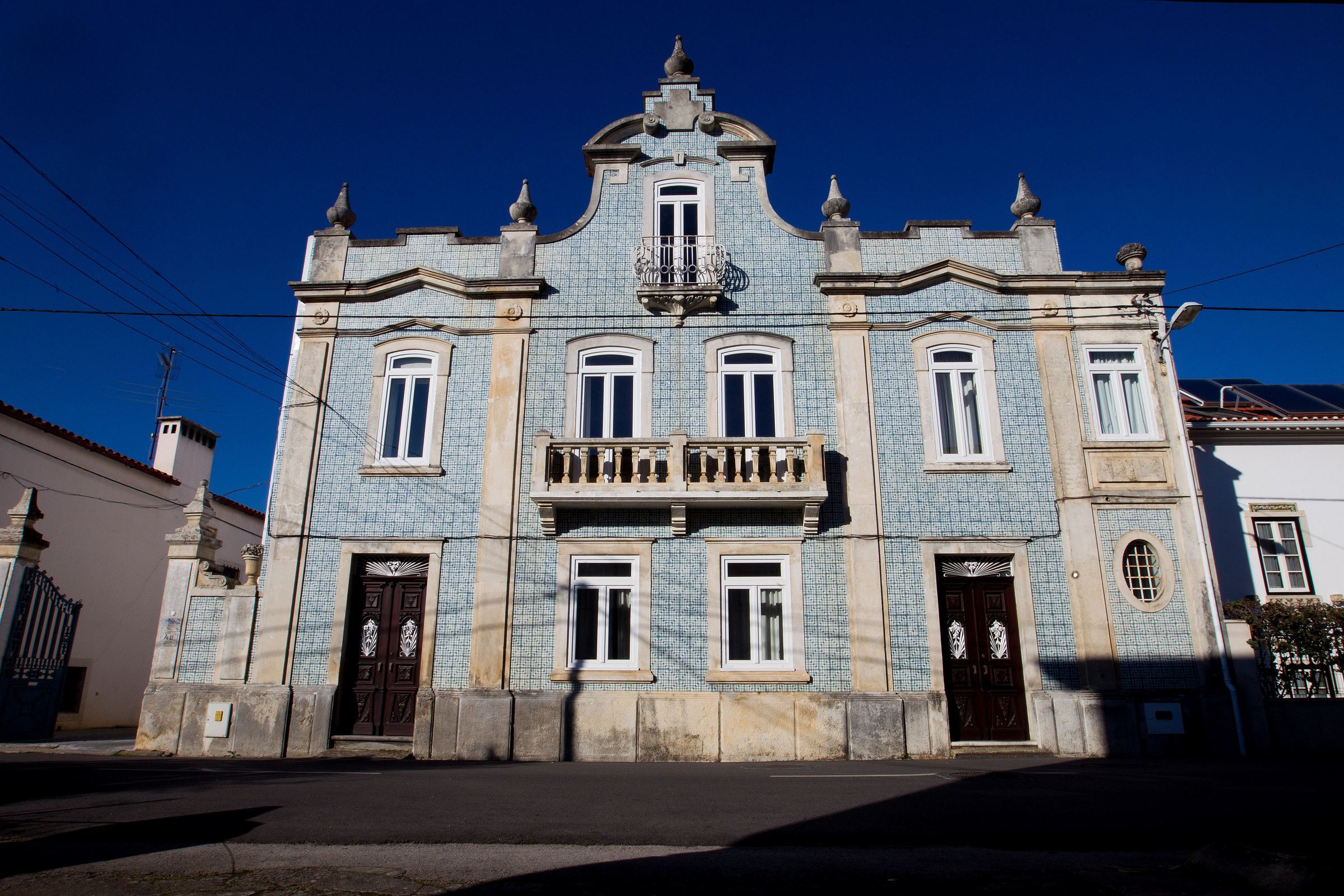 A fachada de azulejo da casa, com varanda de ferro e janela redonda, sob o céu azul-escuro do fim da tarde