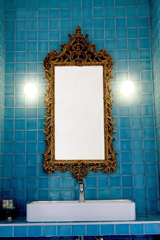Casa de banho revestida a azulejo azul, com um espelho dourado de moldura trabalhada sobre o lavatório