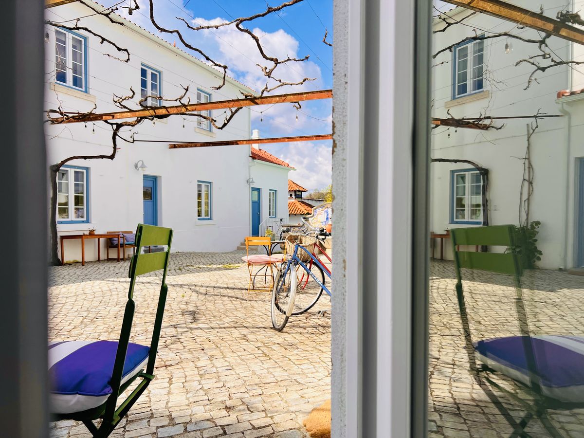 O pátio visto da porta do quarto, com a mesa e as cadeiras à sombra da parreira