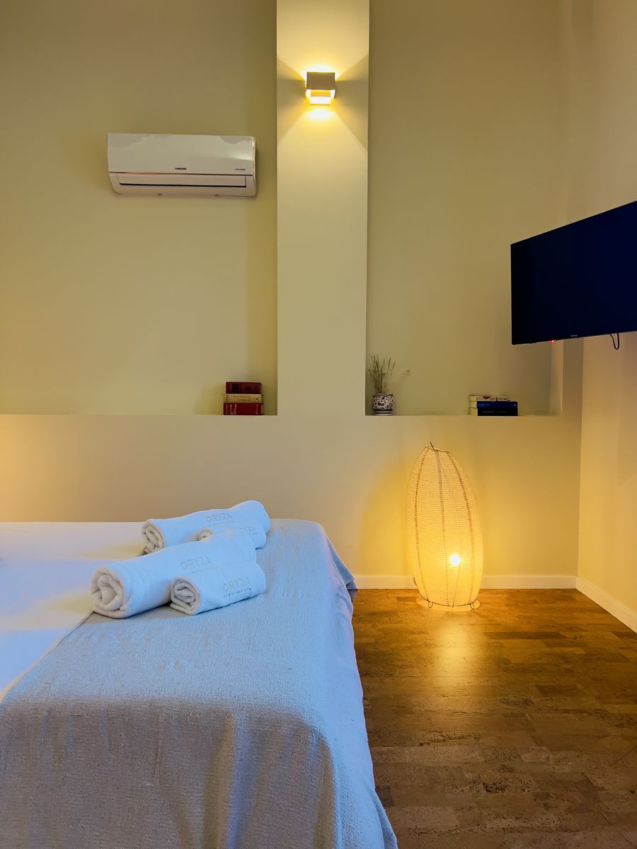A cama do quarto, com toalhas dobradas e candeeiro de pé aceso